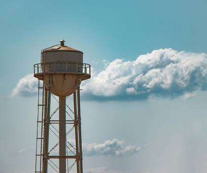 Torre de agua oxidada contra un cielo celeste con una nube