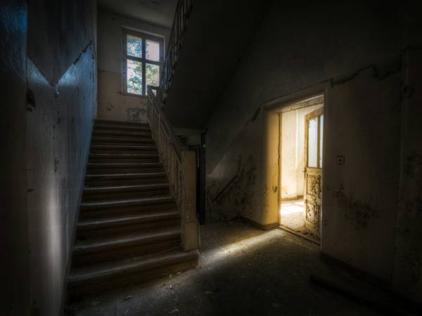 Escalera en penumbra y una puerta abierta que deja entrar la luz