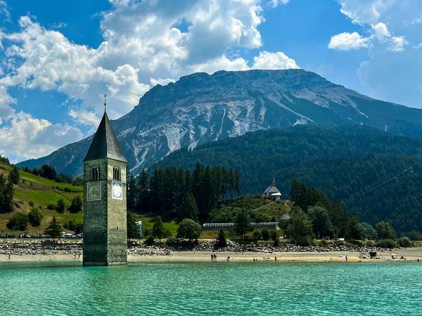 Torre de iglesia en un lago de aguas turquesas, con una montaña de fondo