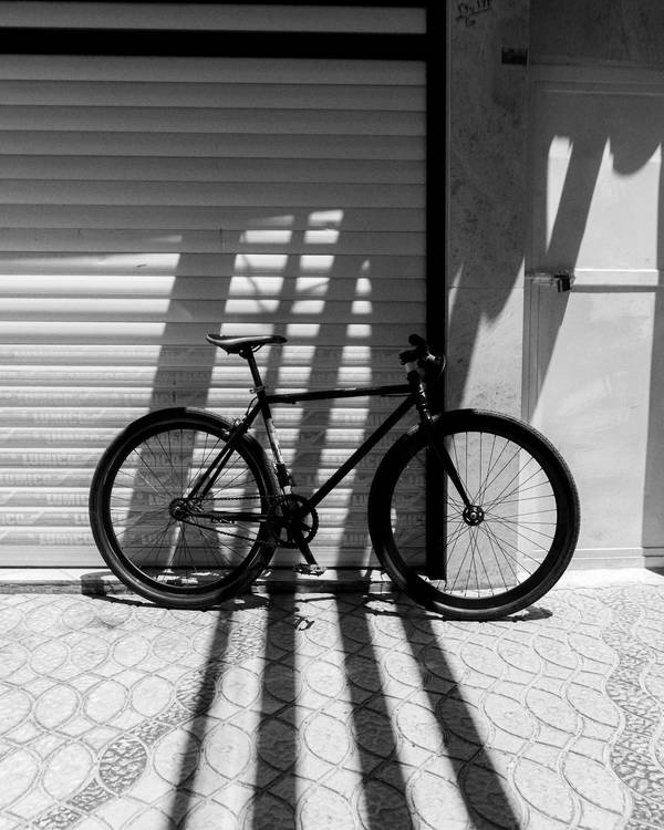 Bicicleta negra apoyada en una cortina metálica, con sombras largas en el suelo