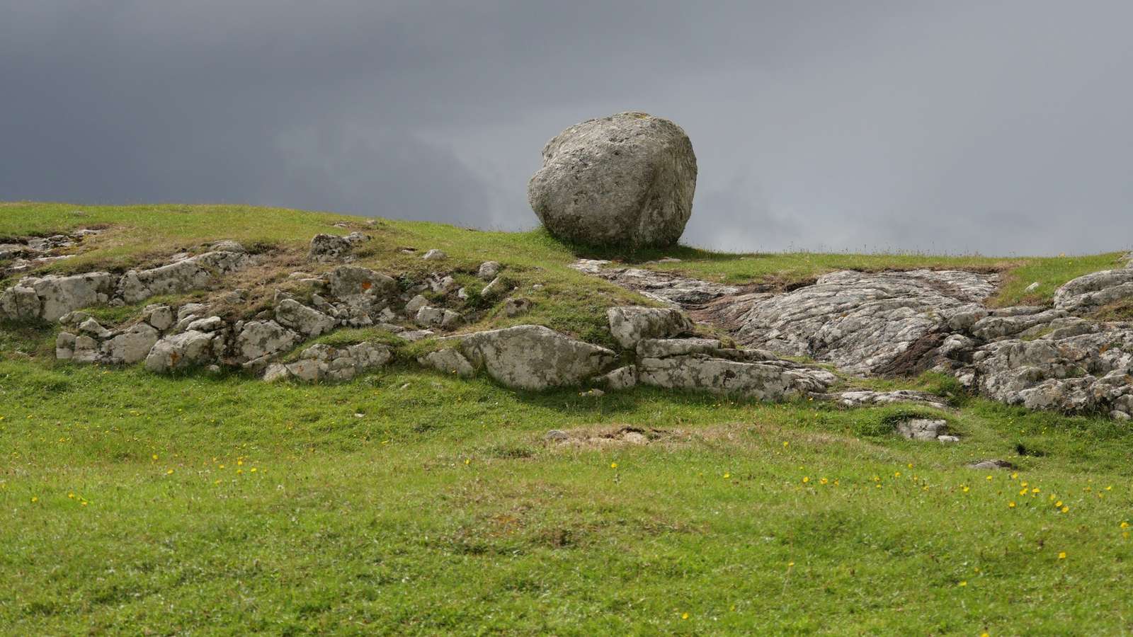 Una roca redonda sobre un afloramiento en una ladera verde