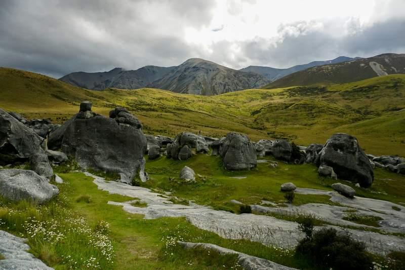 Bloques de piedra gris sobre una ladera verde con montañas al fondo