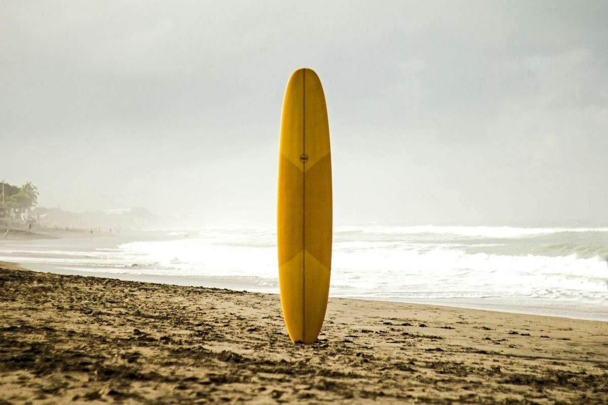 Tabla de surf amarilla clavada en la arena