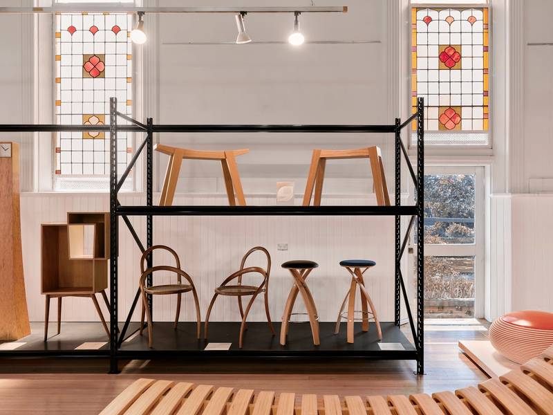Taburetes de madera sobre estantes metálicos junto a vitrales