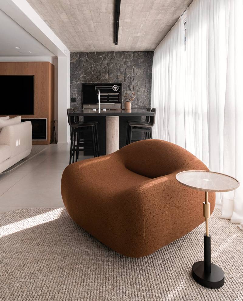 Sillón de forma suave color terracota junto a un ventanal con cortinas