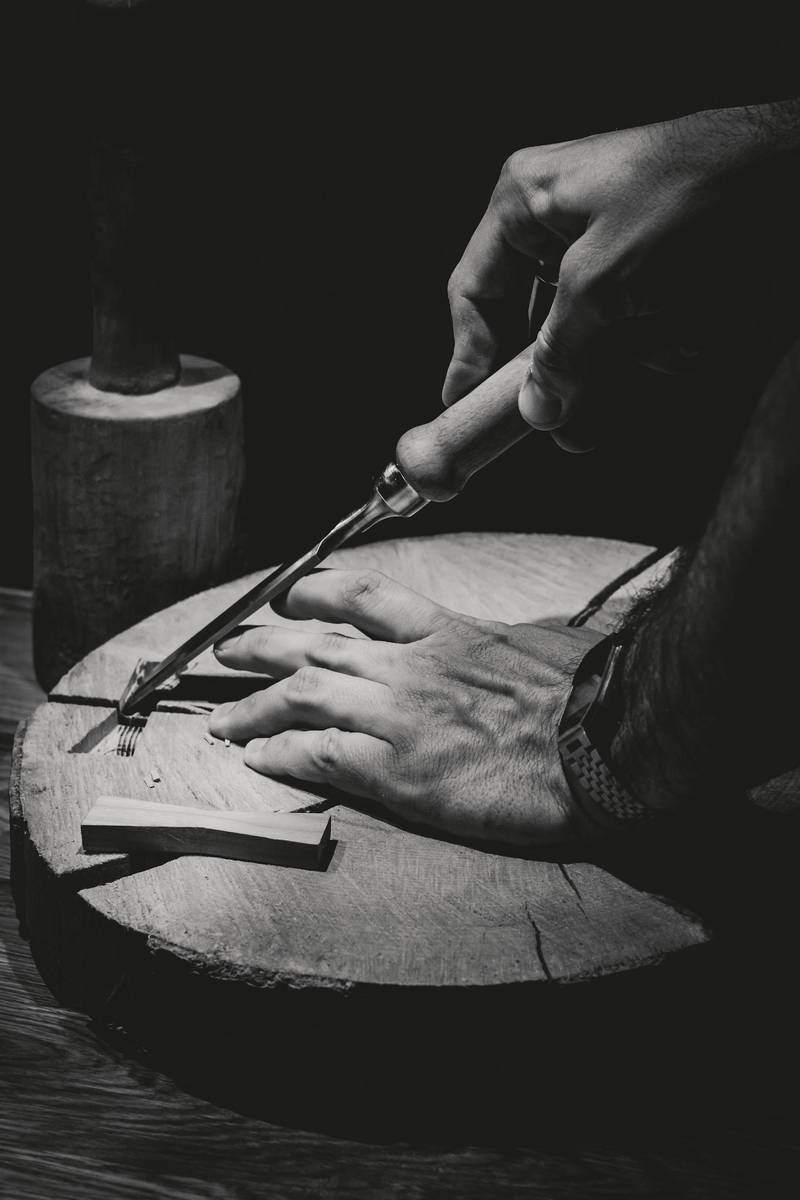 Manos tallando una pieza de madera, en blanco y negro