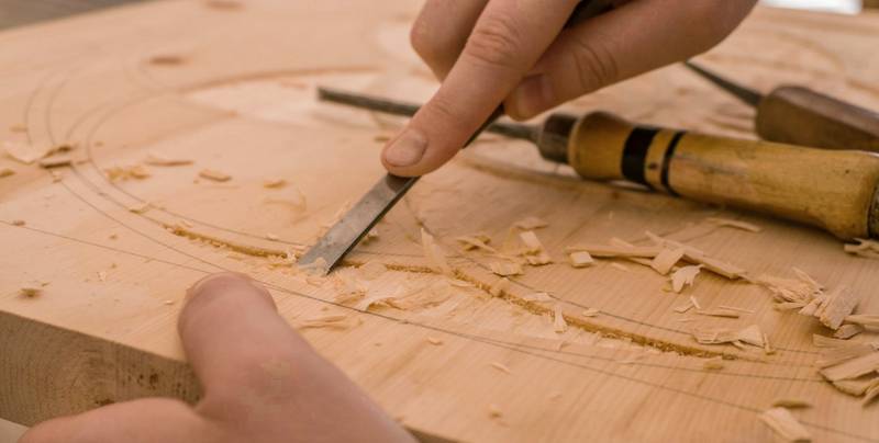 Mano trazando una talla con un formón sobre madera clara