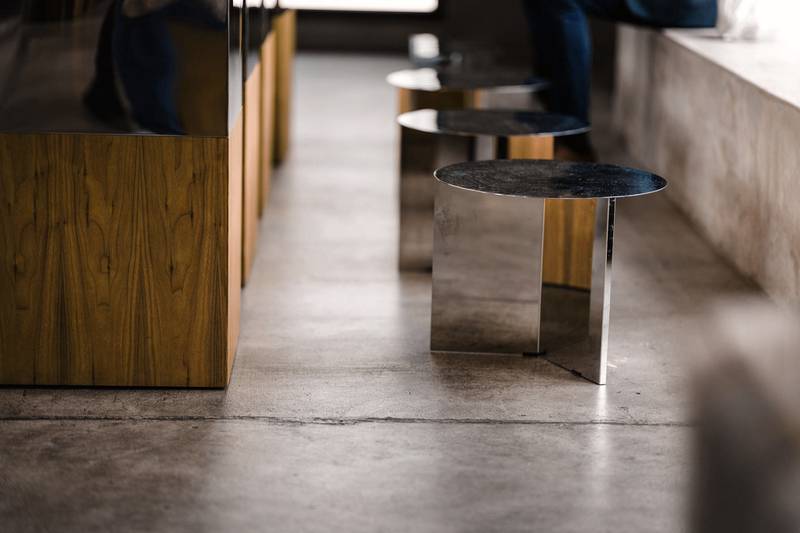 Mesa baja de acero pulido junto a una barra de madera sobre un piso de cemento