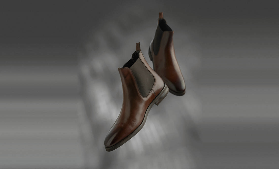 Botines de cuero marrón con elástico, flotando sobre un fondo gris desenfocado