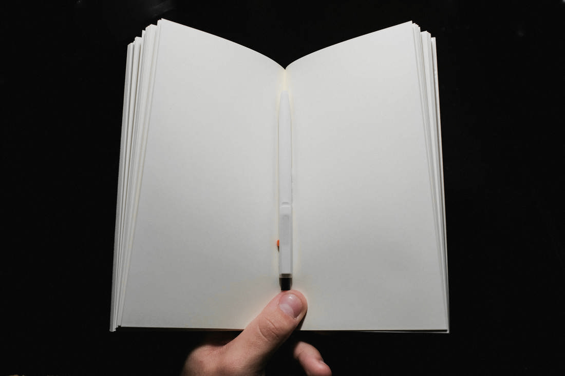 Cuaderno abierto sostenido con una mano sobre fondo negro, con un lápiz entre las páginas