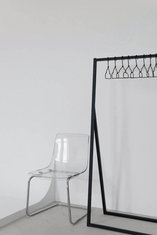 Silla transparente junto a un perchero negro en un rincón blanco
