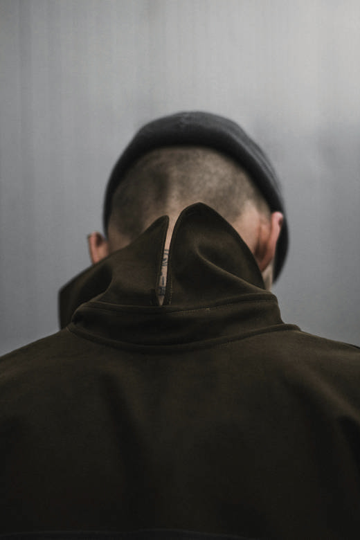 Nuca rapada bajo un gorro oscuro y cuello alto de una chaqueta verde oliva oscuro