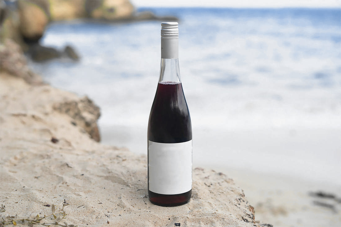 Botella con etiqueta blanca sobre una roca de arena, frente al mar