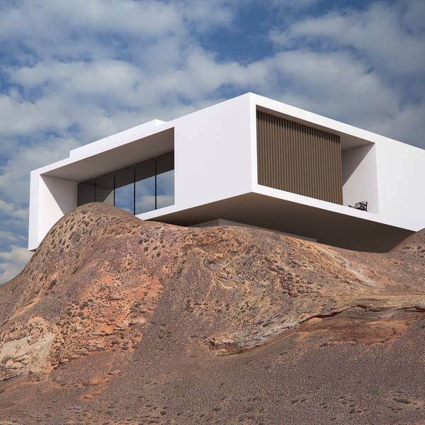 Una casa blanca de volúmenes simples sobre una roca rojiza, bajo un cielo con nubes