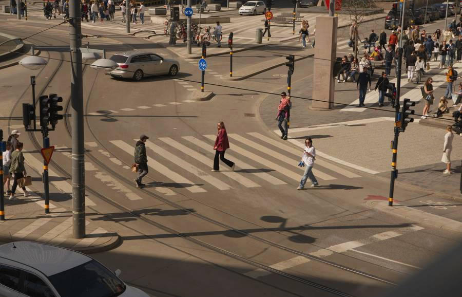 Vista desde lo alto de un cruce peatonal con gente cruzando y un auto, a la luz dorada del atardecer