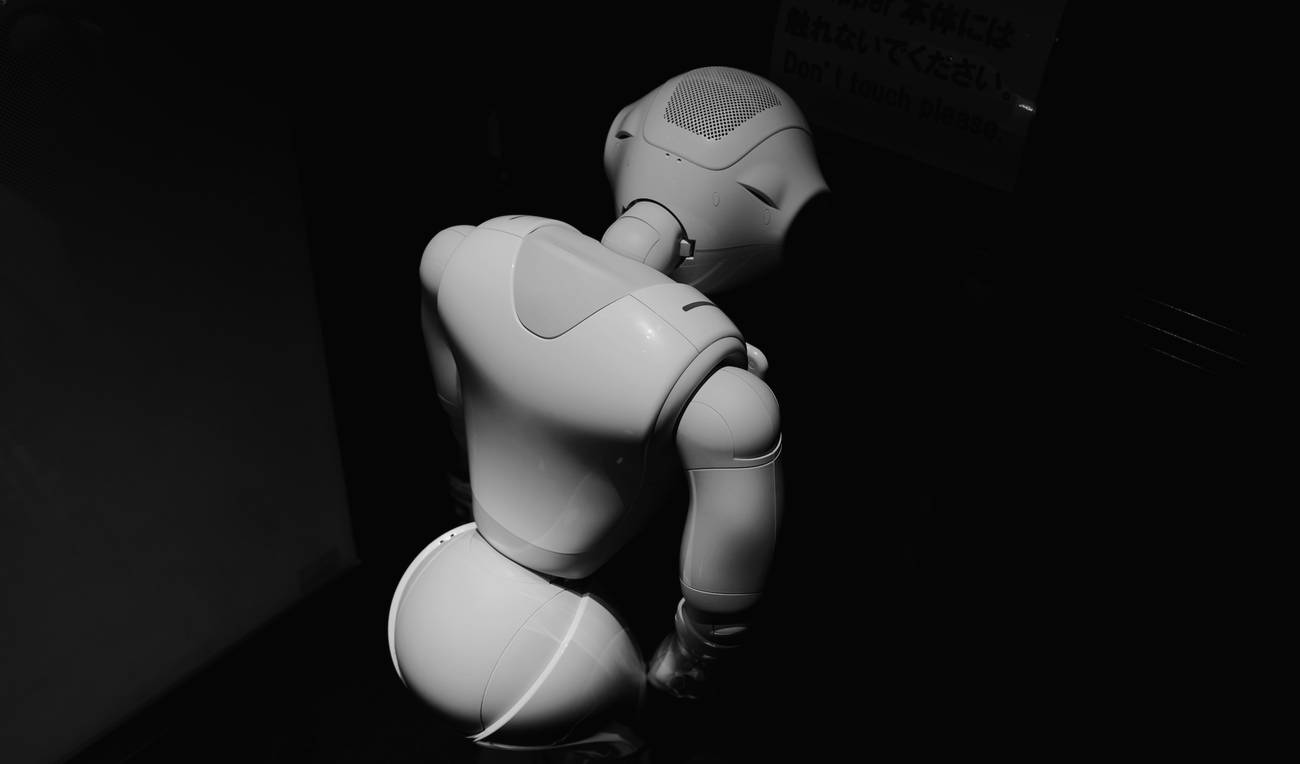 Un robot blanco inclinado en la penumbra, con la luz recortando sus formas