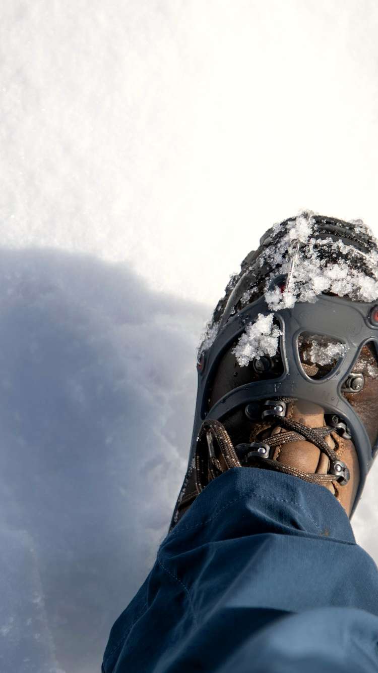 Bota con un crampón de metal sobre la nieve, con la sombra de quien la calza