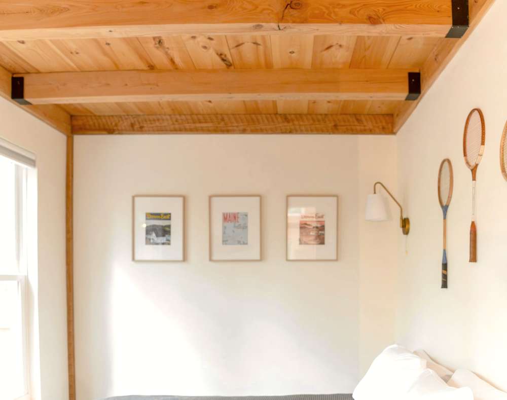 Sala clara con vigas de madera, tres cuadros y raquetas colgadas en la pared