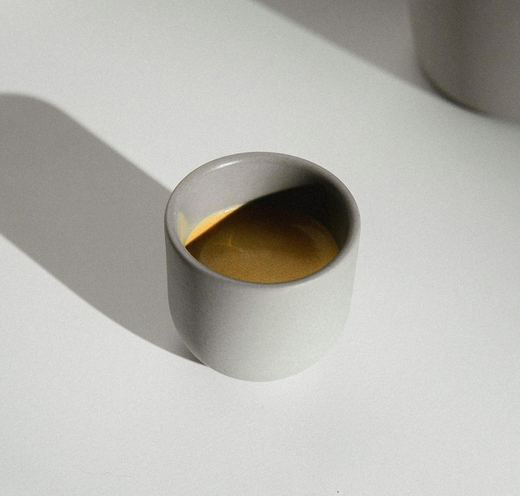 Una taza de espresso gris sobre una mesa blanca, con su sombra alargada