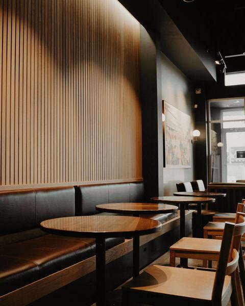 Salón del local con una pared de listones de madera y mesas redondas
