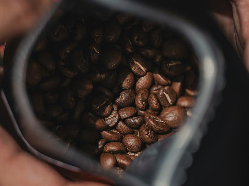Manos sostienen abierta una bolsa de granos de café tostados