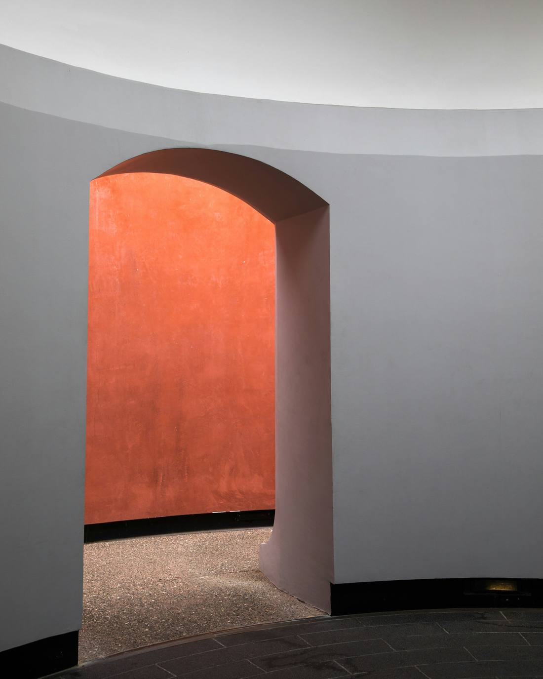 Arco en un muro curvo que deja ver una pared bermellón