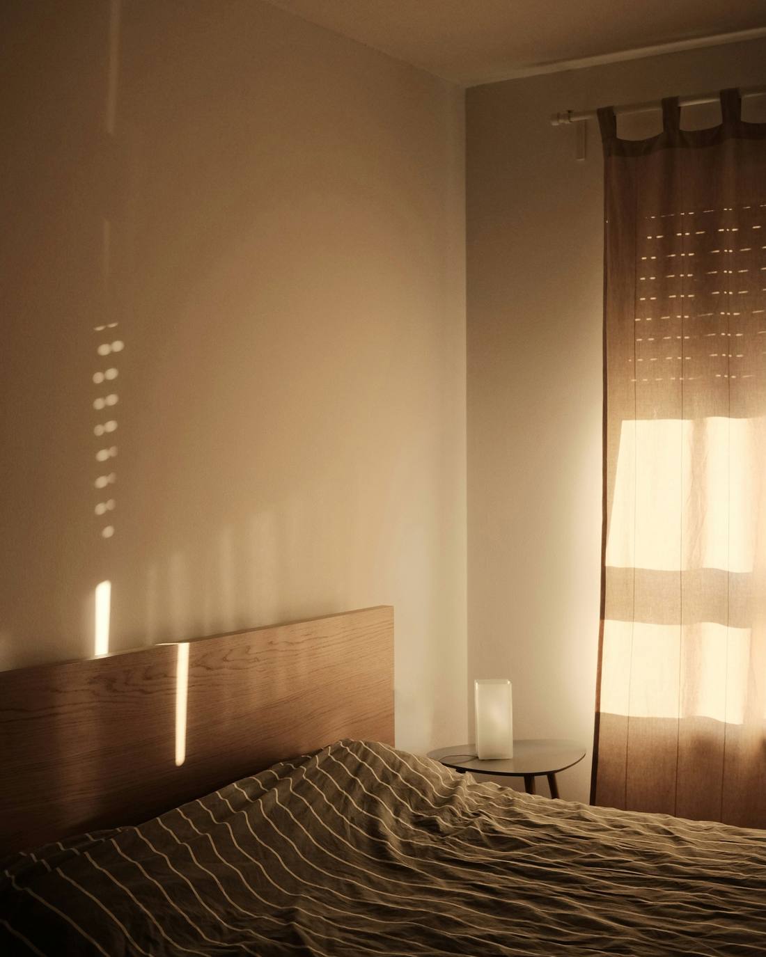 Dormitorio con cabecera de madera y la luz de la tarde en la cortina