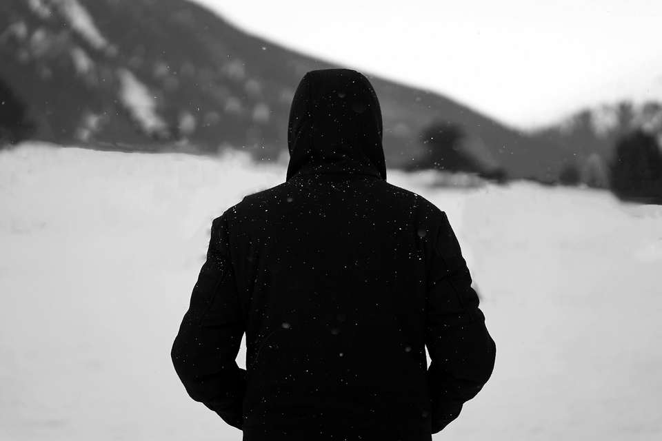 Figura de espaldas con capucha negra en un campo nevado