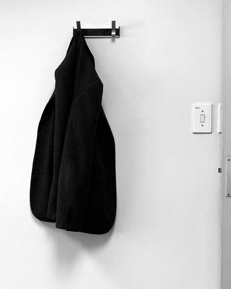 Chaqueta negra colgada de un gancho en una pared blanca
