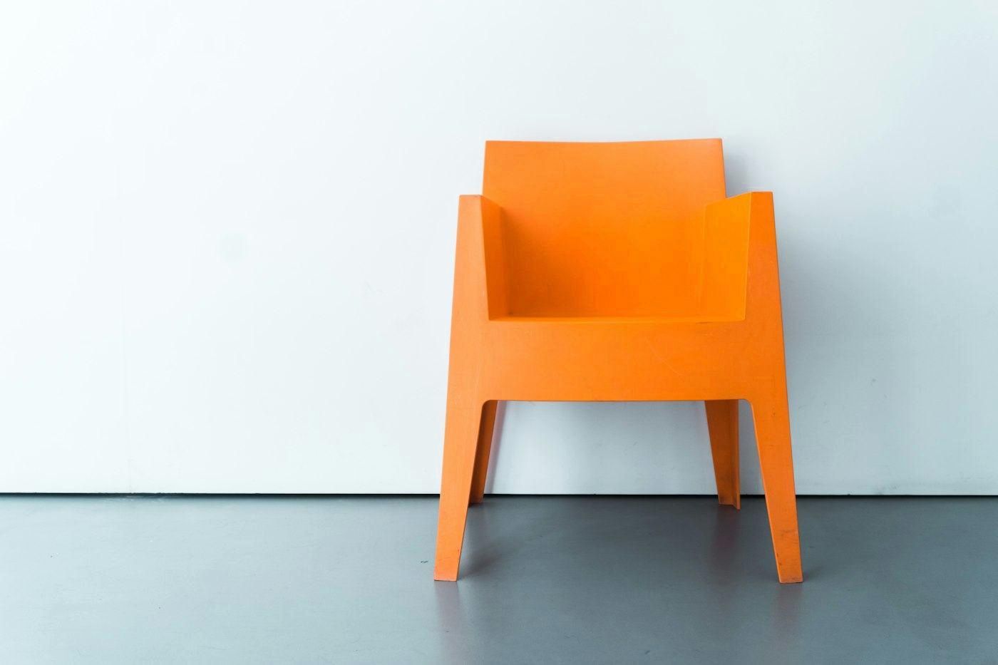 Silla naranja de una sola pieza contra una pared celeste