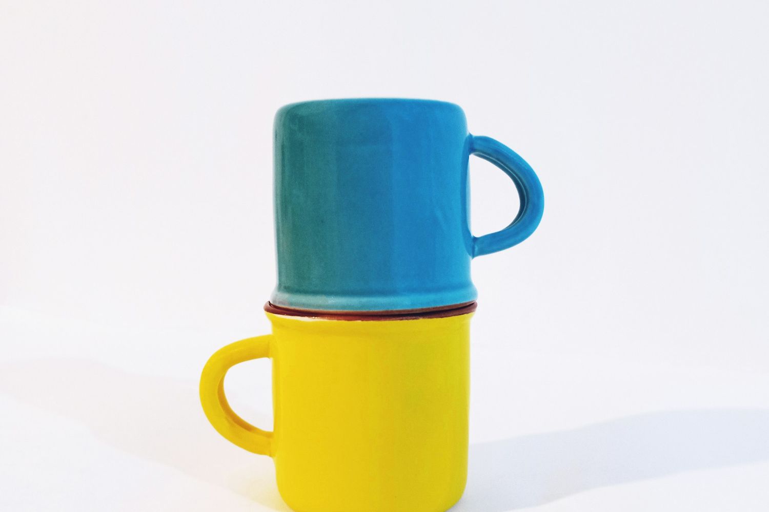 Una taza azul apilada sobre una taza amarilla, sobre fondo claro