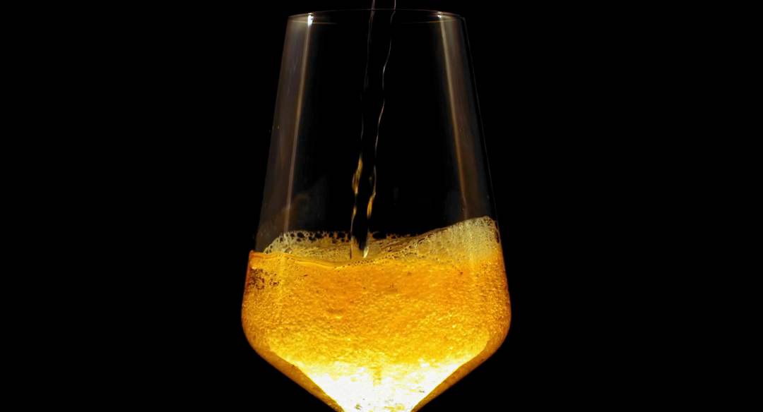 Cerveza dorada que se sirve en una copa sobre un fondo oscuro