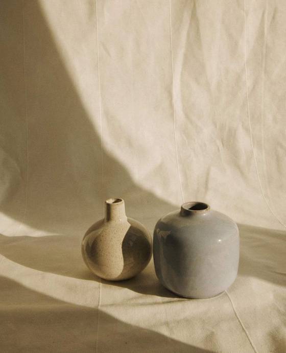 Dos botellas de cerámica, una beige y una gris, sobre una tela arrugada