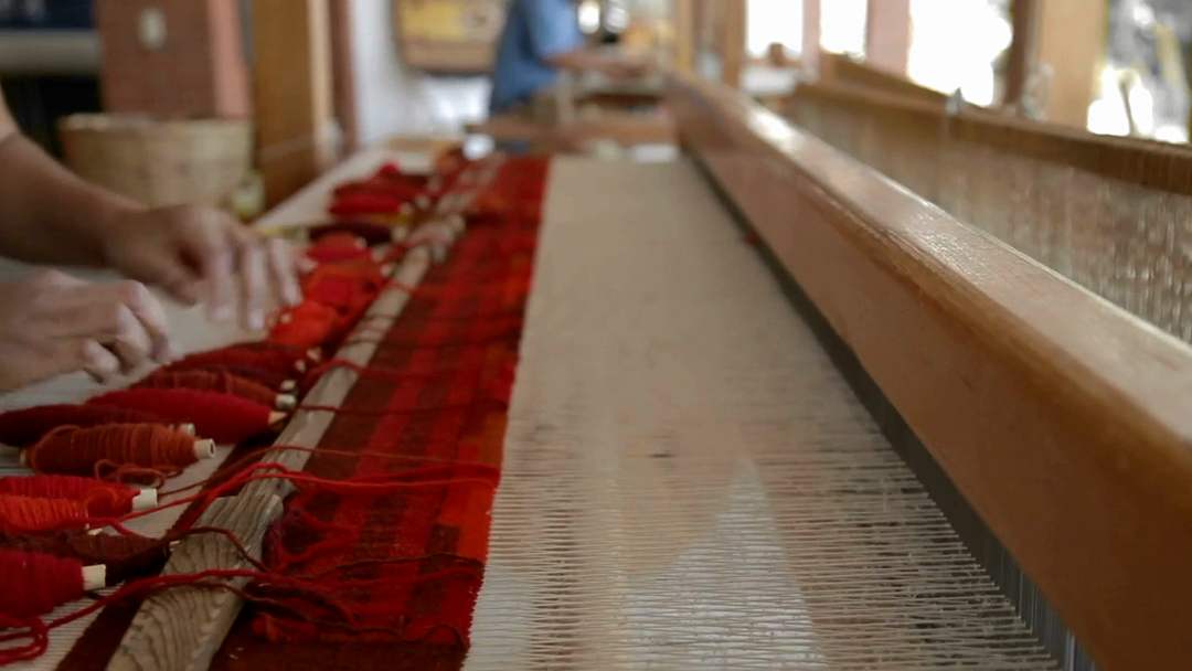 Un telar de madera con la urdimbre tensada y una mano que pasa la trama