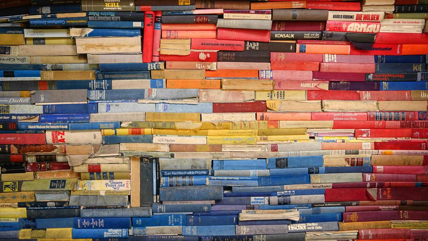 Pared de lomos de libros de muchos colores, apilados en horizontal