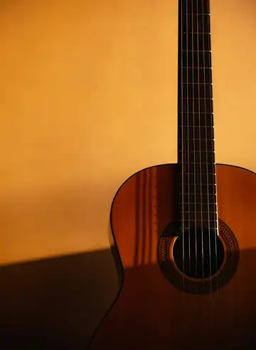 Guitarra clásica apoyada contra una pared amarilla